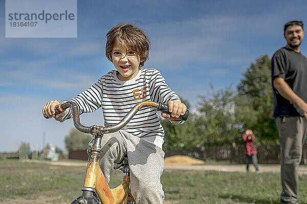 Lächelnder Junge  der an einem sonnigen Tag mit seinem Vater Fahrrad fährt