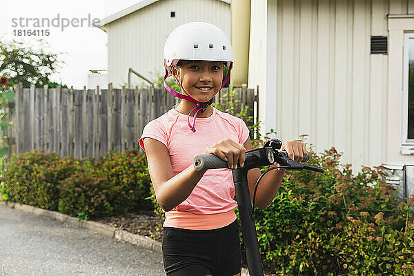 Lächelndes Mädchen mit Helm steht mit Push-Scooter