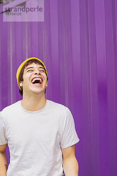 Fröhliche nicht-binäre Person  die vor einer lila Wand lacht