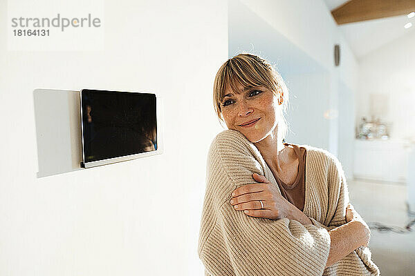 Frau umarmt sich zu Hause in der Nähe eines Tablet-PCs an der Wand