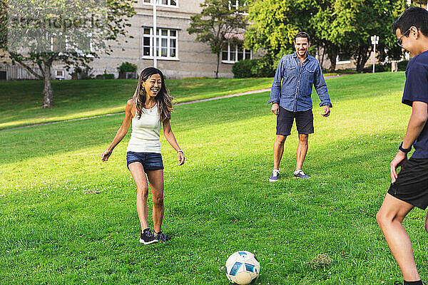 Glückliche Familie  die Fußball auf Gras im Rasen spielt