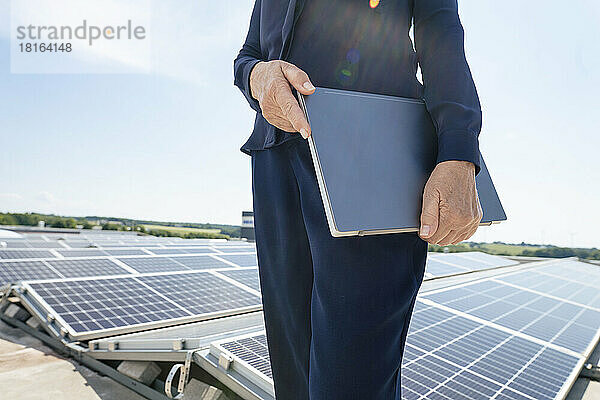 Hände einer Geschäftsfrau  die einen Laptop vor Sonnenkollektoren hält