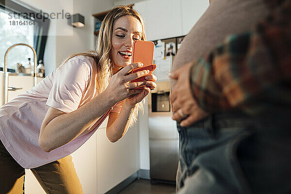 Frau fotografiert schwangeren Bauch ihrer Schwester zu Hause per Smartphone