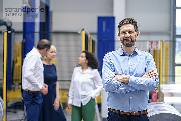 Lächelnder Geschäftsmann steht mit Kollegen im Hintergrund in der Fabrik