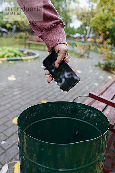 Hand eines Mannes wirft Mobiltelefon in Mülltonne