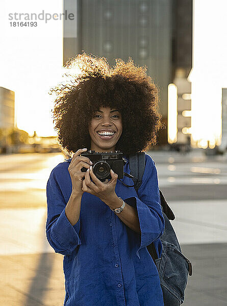 Fröhliche Afro-Frau hält Kamera auf Fußweg