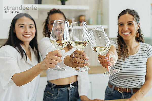 Cheerful young roommates toasting wineglasses in kitchen at home