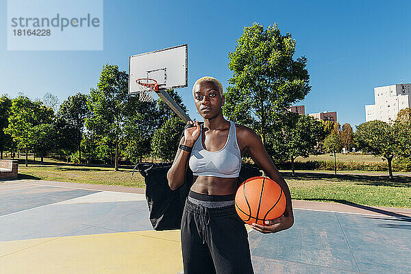 Selbstbewusster Basketballspieler mit Sportball auf dem Platz an einem sonnigen Tag