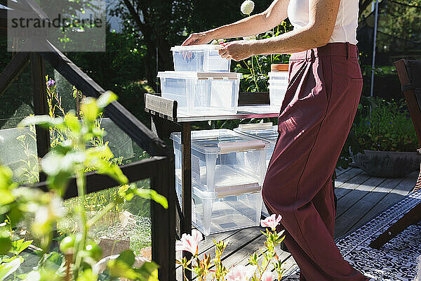 Hände einer Frau  die Plastikbehälter auf dem Tisch auf der Terrasse arrangiert