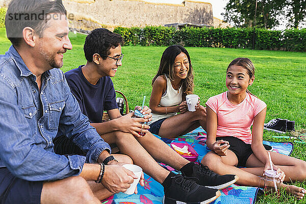 Gemischtrassige Familie genießt Getränke im Rasen beim Picknick