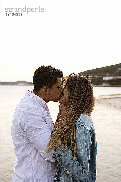 Romantisches Paar küsst sich am Strand bei Sonnenuntergang
