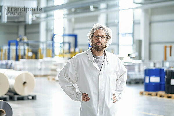Mann im Laborkittel steht mit den Händen auf der Hüfte in der Industrie