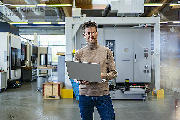 Lächelnder reifer Geschäftsmann mit Laptop in der Industrie