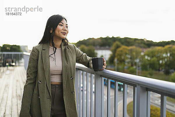 Nachdenkliche Frau mit Kaffeetasse steht auf der Terrasse