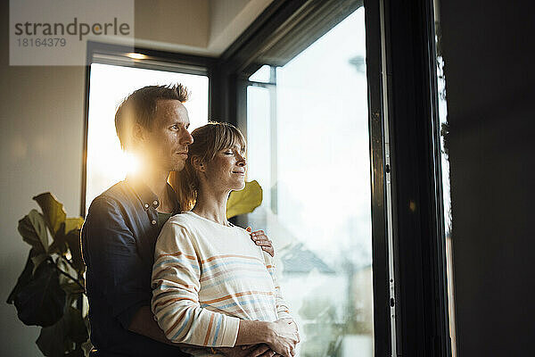 Expectant couple standing together near glass door at home