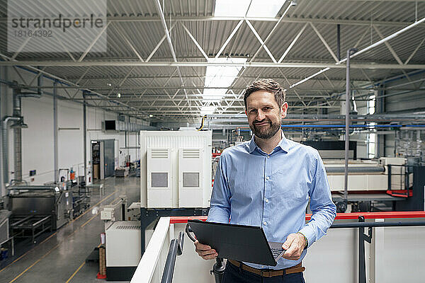 Lächelnder Geschäftsmann mit Laptop in der Industrie