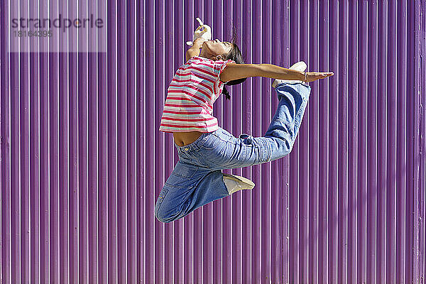 Junge Frau springt vor violetter Wellwand