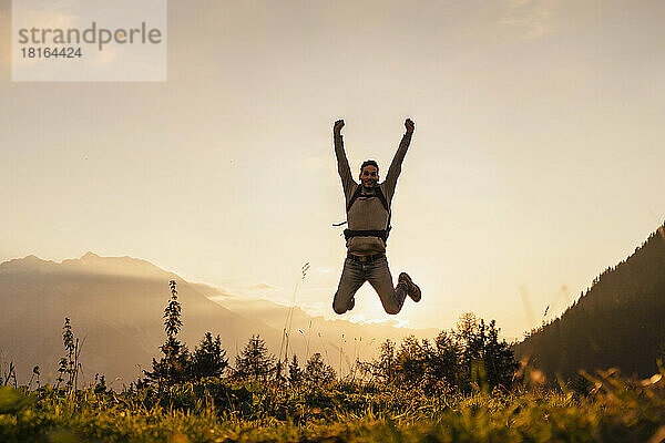 Glücklicher Mann springt bei Sonnenuntergang auf den Gipfel des Berges