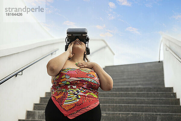 Lächelnde Frau mit Virtual-Reality-Simulator vor der Treppe