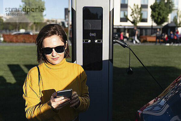 Frau mit Sonnenbrille benutzt Mobiltelefon an Ladestation