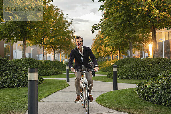 Fröhlicher Pendler fährt Fahrrad auf Fußweg im Park