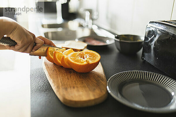 Hände einer Frau  die zu Hause in der Küche Orangenfrüchte mit einem Messer schneidet