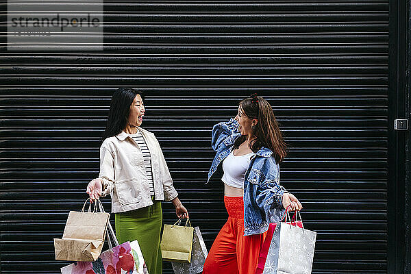Cheerful lesbian couple with shopping bags in front of shutter