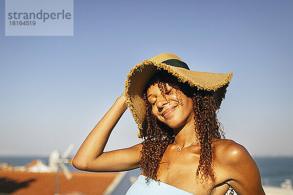 Lächelnde Frau mit geschlossenen Augen und Hut an einem sonnigen Tag