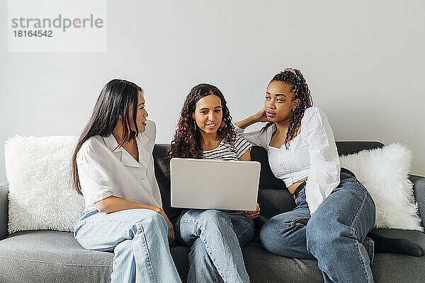 Young woman with laptop sitting amidst multiracial roommates in living room