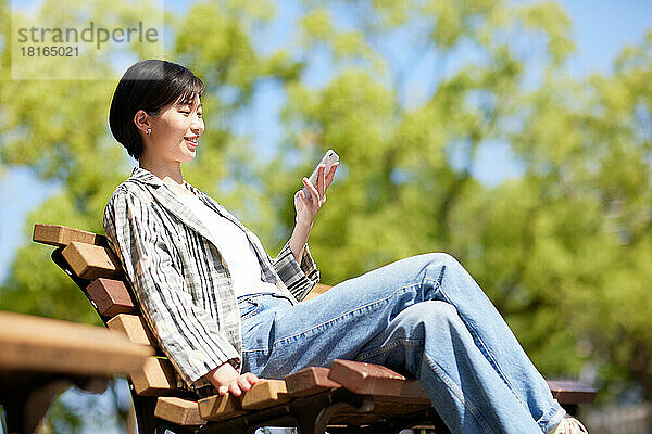 Junge Japanerin benutzt Smartphone in einem Stadtpark