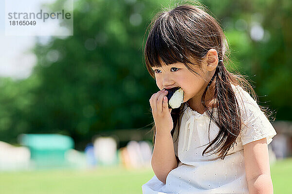 Japanisches Kind isst in einem Stadtpark