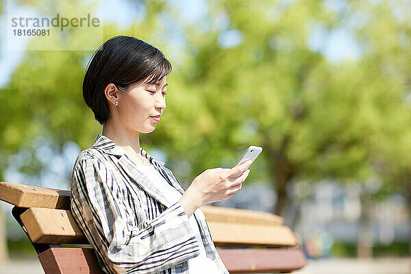 Junge Japanerin benutzt Smartphone in einem Stadtpark