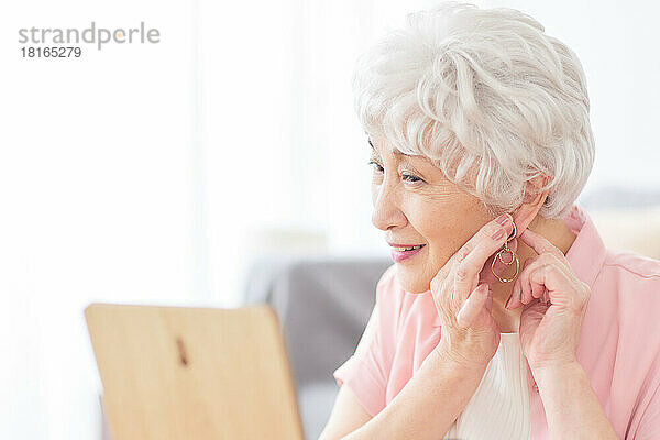 Japanische Seniorin beim Anlegen von Ohrringen