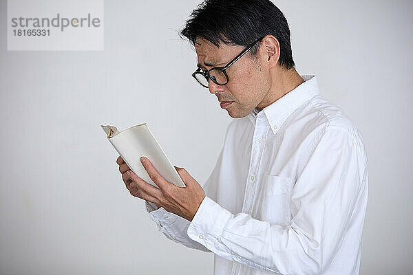 Japaner  der an Alterssichtigkeit leidet  hat Schwierigkeiten beim Lesen von Büchern