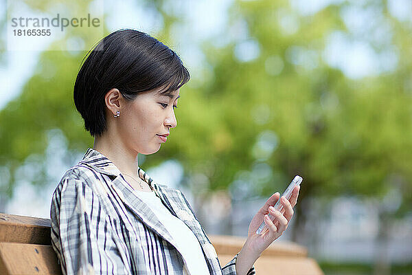 Junge Japanerin benutzt Smartphone in einem Stadtpark