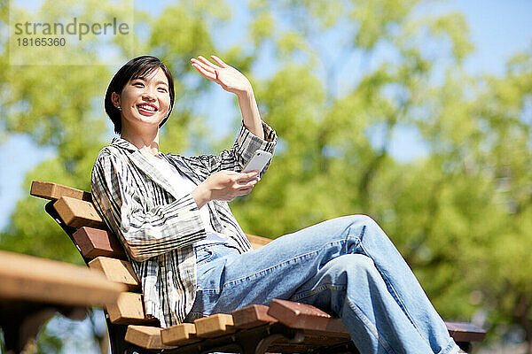 Junge Japanerin benutzt Smartphone in einem Stadtpark