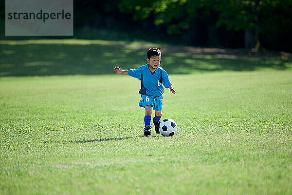 Japanisches Kind spielt Fußball in einem Stadtpark