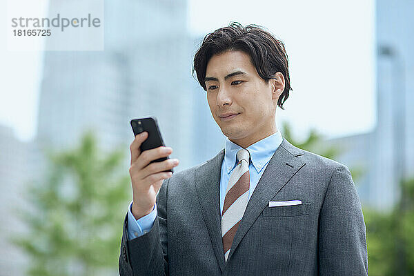 Japanischer Geschäftsmann blickt auf Smartphone