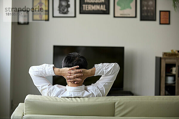 Rückansicht eines japanischen Mannes  der es sich auf dem Sofa gemütlich macht