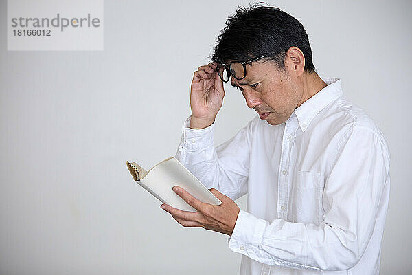 Japaner  der an Alterssichtigkeit leidet  hat Schwierigkeiten beim Lesen von Büchern