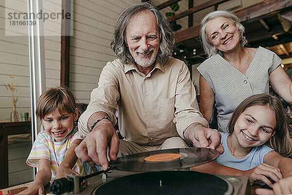 Lächelnder Großvater wechselt zu Hause von seinen Enkelinnen die Schallplatte auf dem Plattenspieler