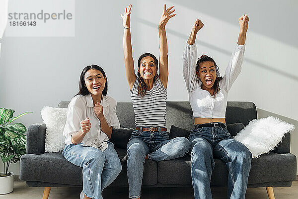 Cheerful friends celebrating together sitting on sofa at home