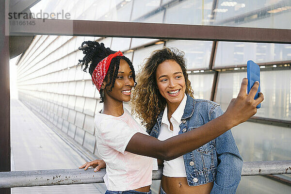 Lächelnde  gemischtrassige Frauen  die am Geländer ein Selfie mit dem Mobiltelefon machen