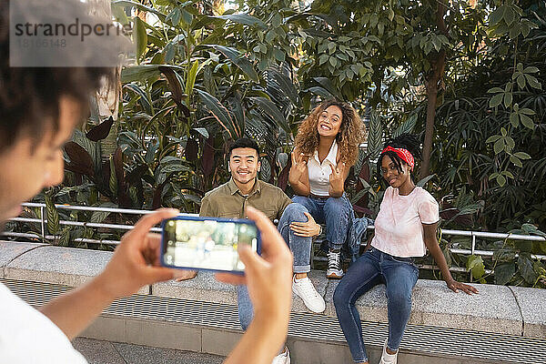 Junger Mann fotografiert lächelnde Freunde mit Smartphone an der Wand