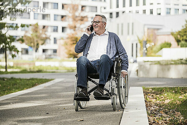 Lächelnder älterer Mann  der im Rollstuhl sitzt und mit dem Mobiltelefon spricht