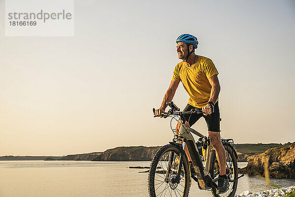 Reifer Mann fährt bei Sonnenuntergang Fahrrad am Ufer
