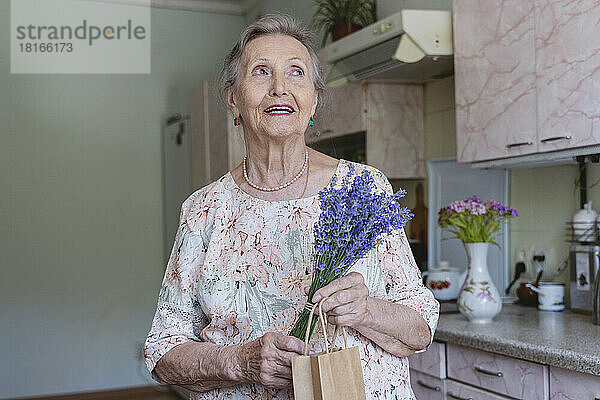 Glückliche ältere Frau mit einem Strauß Lavendelblüten träumt in der heimischen Küche