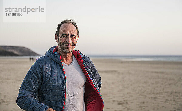 Lächelnder Mann in Jacke vor dem Himmel am Strand