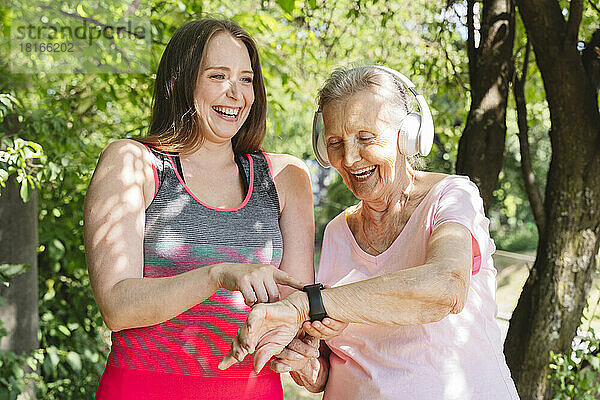 Fröhlicher Fitnesstrainer mit Seniorin mit Smartwatch im Park