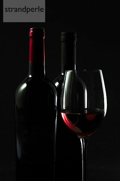 Dunkle Studioaufnahme von Flaschen und einem Glas Rotwein